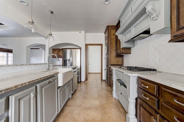 kitchen with decorative backsplash, appliances with stainless steel finishes, light stone counters, a sink, and light tile patterned flooring