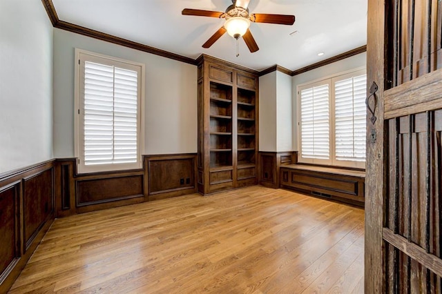 interior space featuring ornamental molding, a wainscoted wall, and light wood-style floors