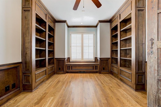 empty room with a wainscoted wall, light wood-style flooring, built in shelves, and crown molding