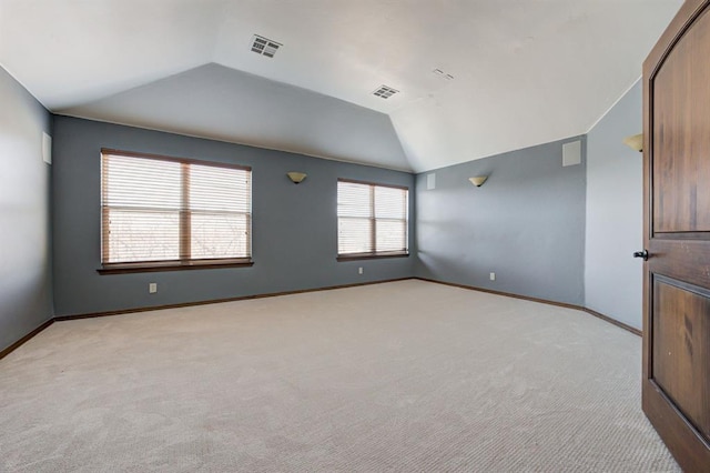 empty room featuring light colored carpet, visible vents, and vaulted ceiling