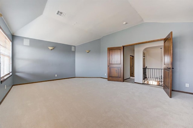 empty room featuring lofted ceiling, baseboards, arched walkways, and light colored carpet