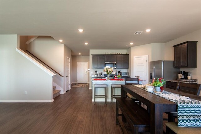 kitchen with dark brown cabinetry, stainless steel appliances, dark wood-type flooring, light countertops, and a center island with sink