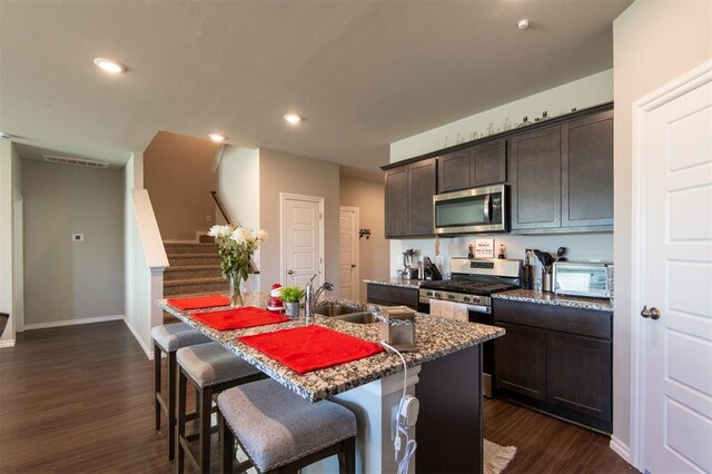 kitchen featuring dark wood finished floors, recessed lighting, appliances with stainless steel finishes, dark brown cabinets, and an island with sink