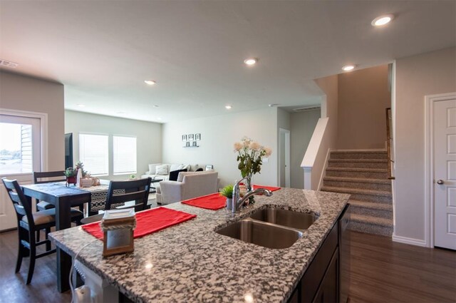 kitchen featuring recessed lighting, a sink, open floor plan, light stone countertops, and an island with sink