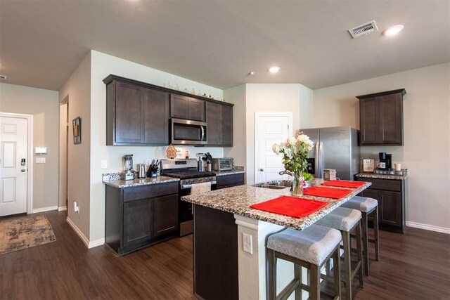 kitchen featuring a center island with sink, visible vents, appliances with stainless steel finishes, a sink, and dark brown cabinets