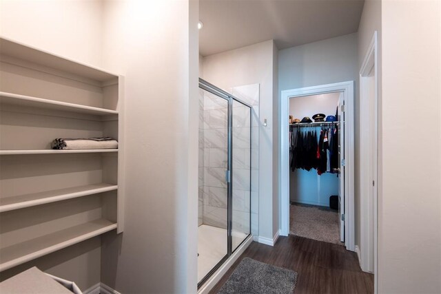 bathroom featuring a stall shower, baseboards, a walk in closet, and wood finished floors