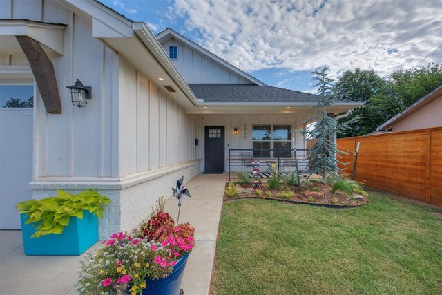 doorway to property featuring board and batten siding, a porch, fence, and a lawn