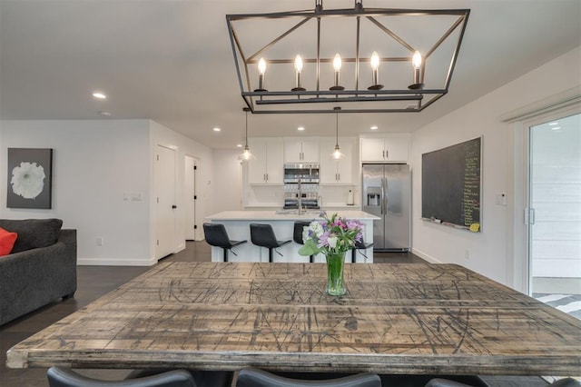 kitchen featuring decorative light fixtures, stainless steel appliances, light countertops, a kitchen island with sink, and white cabinets