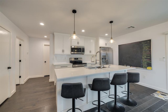 kitchen featuring visible vents, white cabinets, appliances with stainless steel finishes, hanging light fixtures, and a kitchen island with sink