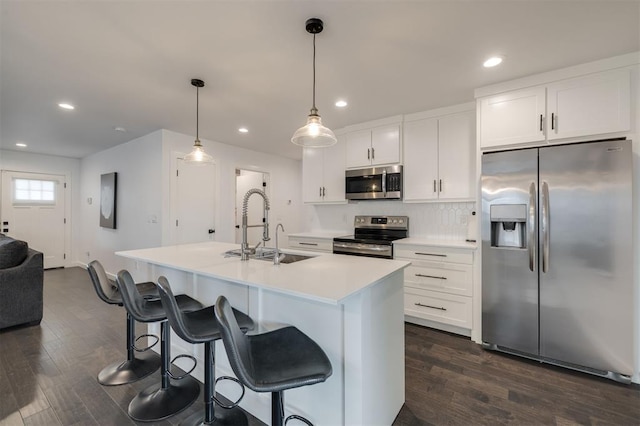 kitchen featuring decorative light fixtures, light countertops, appliances with stainless steel finishes, white cabinetry, and an island with sink