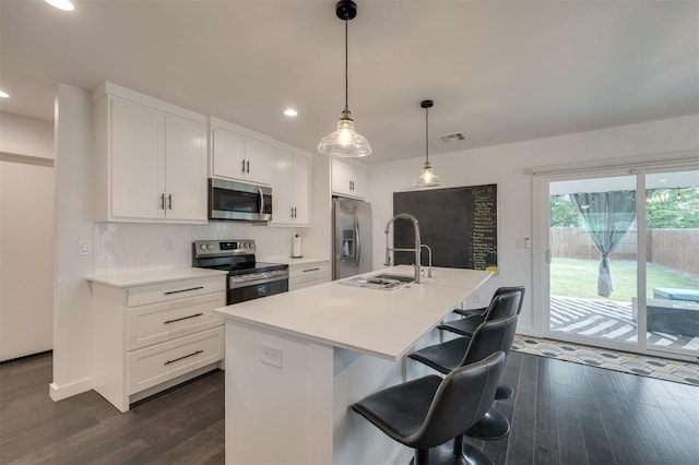 kitchen featuring an island with sink, appliances with stainless steel finishes, pendant lighting, and light countertops