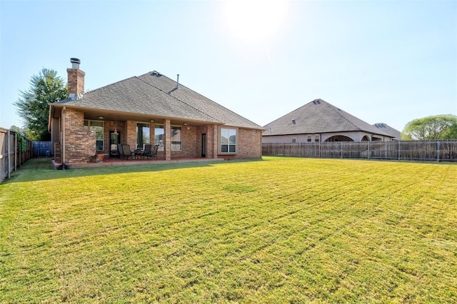 back of property featuring a yard, a fenced backyard, a chimney, and brick siding