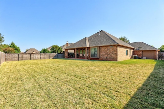 rear view of property featuring cooling unit, a fenced backyard, brick siding, and a lawn