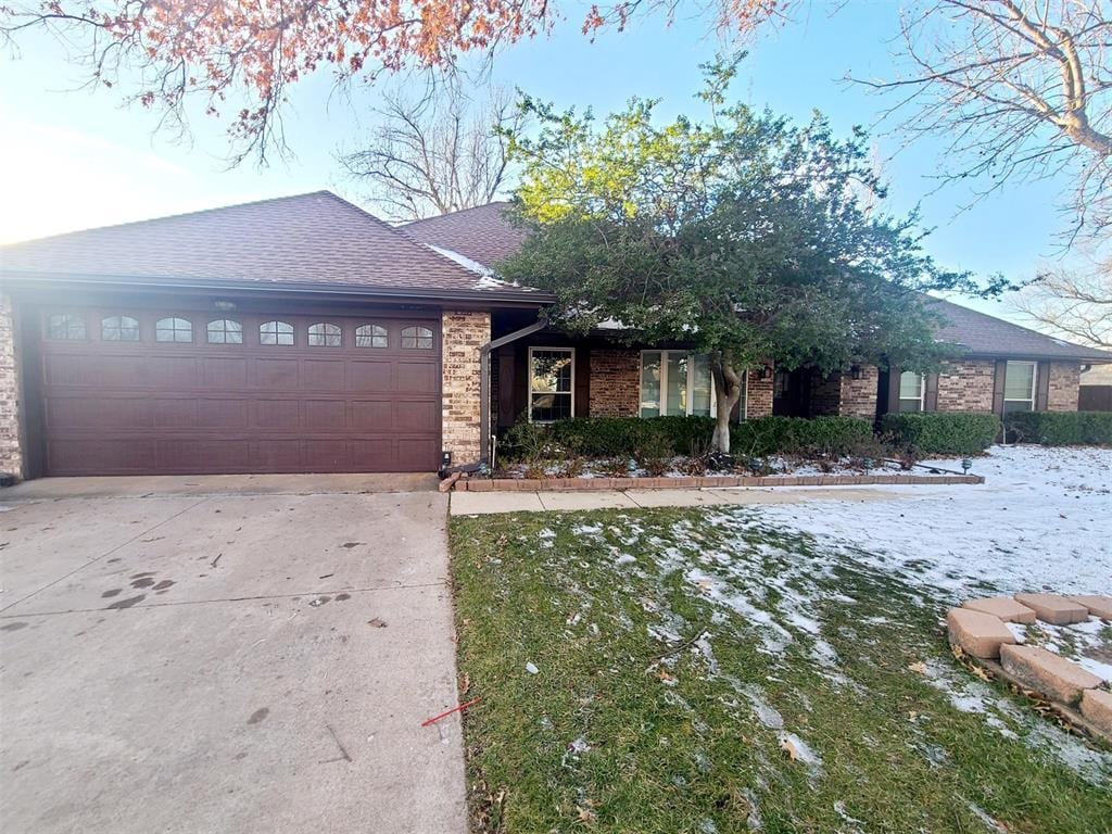 ranch-style house with an attached garage, roof with shingles, concrete driveway, and brick siding