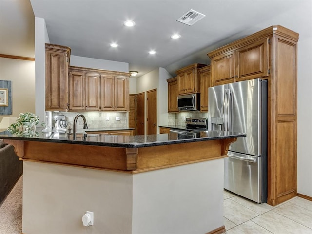 kitchen featuring visible vents, brown cabinetry, dark stone counters, appliances with stainless steel finishes, and a kitchen bar