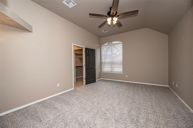 unfurnished bedroom with a walk in closet, visible vents, lofted ceiling, and carpet