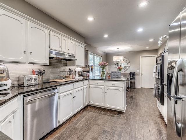 kitchen with under cabinet range hood, stainless steel appliances, a peninsula, white cabinetry, and hanging light fixtures