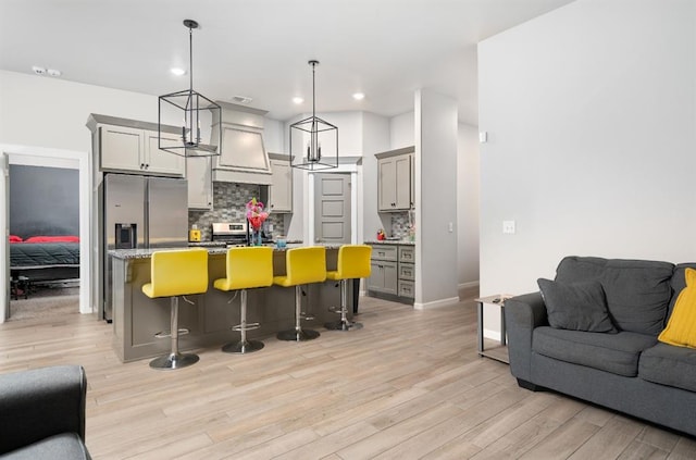 kitchen featuring stainless steel appliances, light wood-style floors, open floor plan, backsplash, and an island with sink