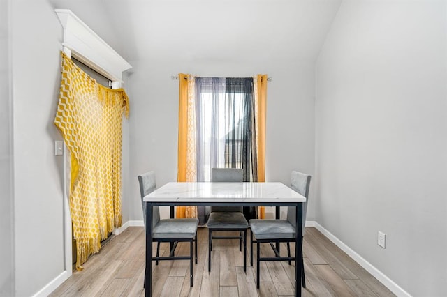 dining area featuring vaulted ceiling, light wood-style flooring, and baseboards