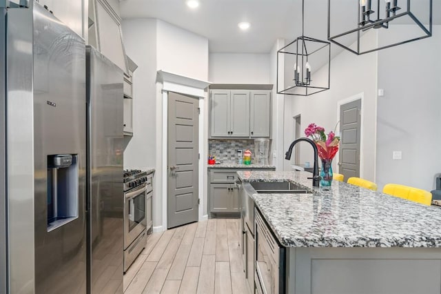 kitchen with light wood finished floors, decorative backsplash, an island with sink, stainless steel appliances, and gray cabinetry