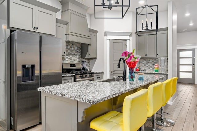 kitchen with light wood-style flooring, a sink, a kitchen breakfast bar, appliances with stainless steel finishes, and custom range hood