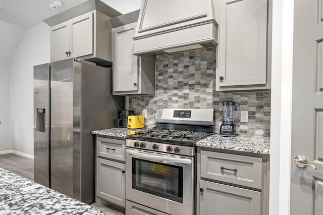 kitchen featuring appliances with stainless steel finishes, premium range hood, light stone counters, and decorative backsplash