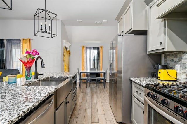 kitchen featuring light wood-style flooring, stainless steel appliances, a sink, backsplash, and light stone countertops