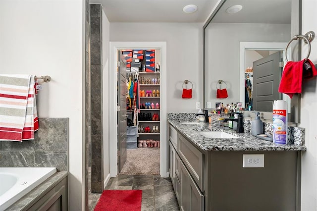 bathroom featuring a spacious closet, a garden tub, and vanity