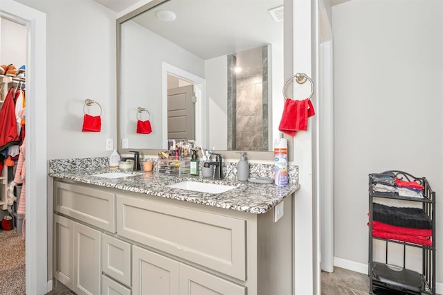 full bath featuring double vanity, a spacious closet, baseboards, and a sink