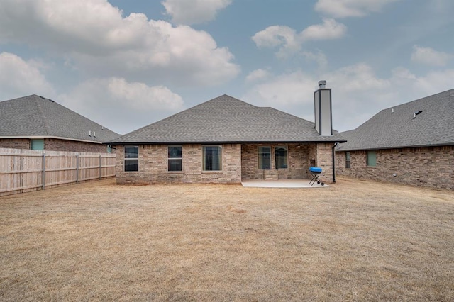 back of property featuring fence private yard, brick siding, roof with shingles, a lawn, and a patio area