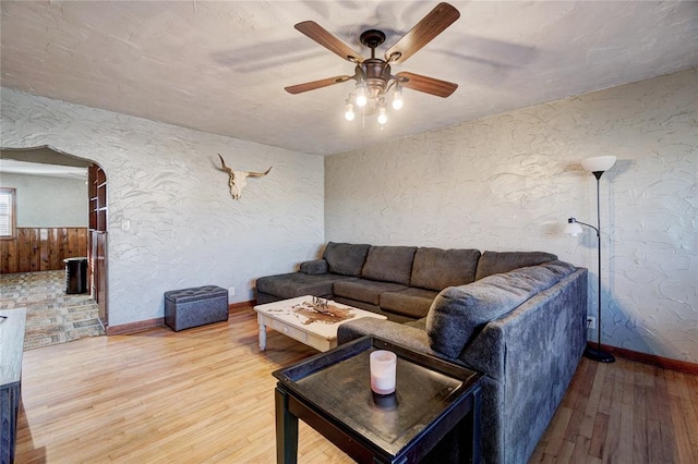 living room with arched walkways, a textured wall, light wood finished floors, and a ceiling fan