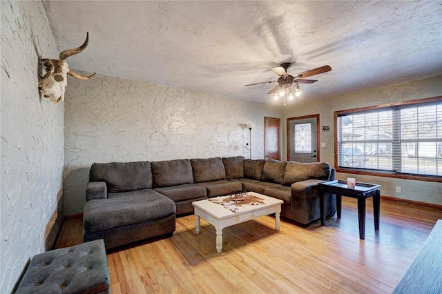 living room with a textured wall, light wood-style flooring, and a ceiling fan