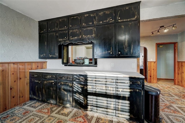 kitchen with wooden walls, a textured wall, wainscoting, light countertops, and backsplash