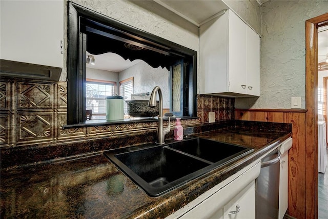 kitchen with a textured wall, a sink, white cabinets, wainscoting, and dishwasher