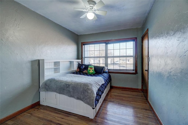 bedroom with baseboards, dark wood finished floors, a ceiling fan, and a textured wall