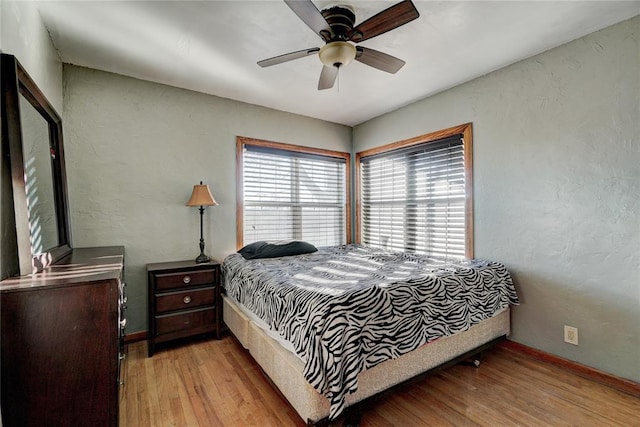 bedroom with a textured wall, light wood-style flooring, baseboards, and ceiling fan