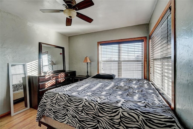 bedroom with light wood-style floors, a ceiling fan, and a textured wall