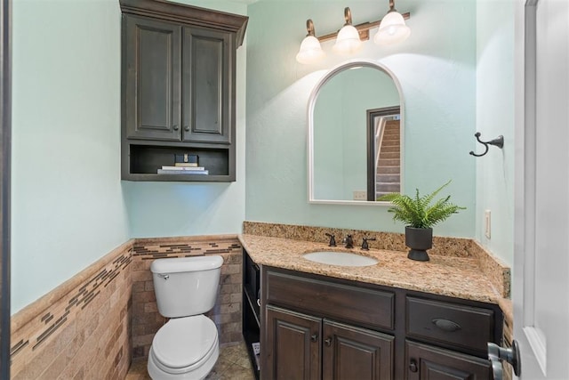 bathroom with toilet, vanity, tile walls, wainscoting, and tile patterned floors