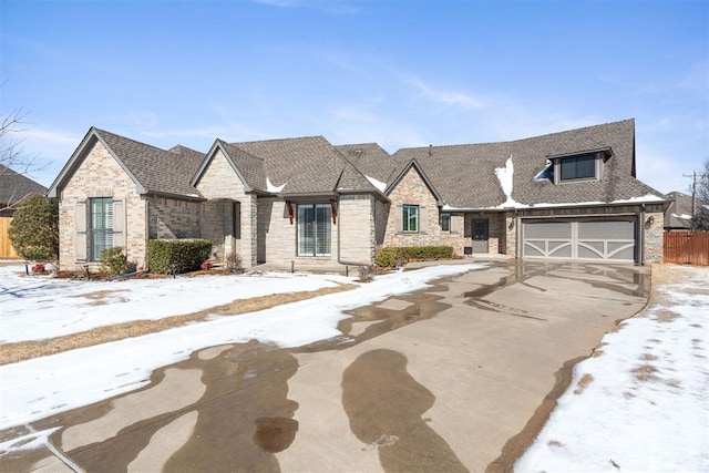 view of front of property featuring a garage, a shingled roof, fence, driveway, and stone siding