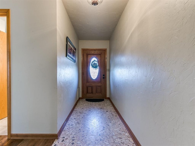 doorway to outside featuring baseboards and a textured wall