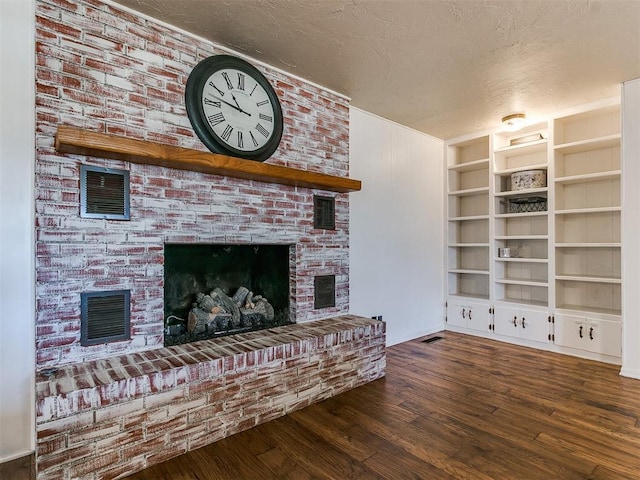 living area featuring a textured ceiling, dark wood-style flooring, a brick fireplace, and visible vents