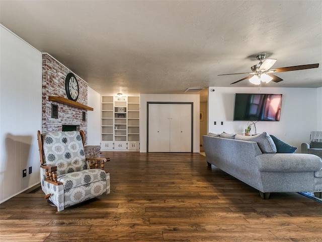 living room with built in features, a fireplace, dark wood-type flooring, ceiling fan, and a textured ceiling