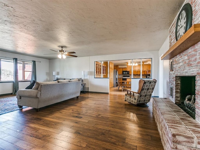 living area with a textured ceiling, a fireplace, dark wood-style flooring, and ceiling fan with notable chandelier