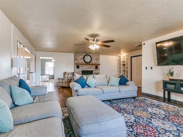 living room with ceiling fan, a textured ceiling, a fireplace, wood finished floors, and baseboards