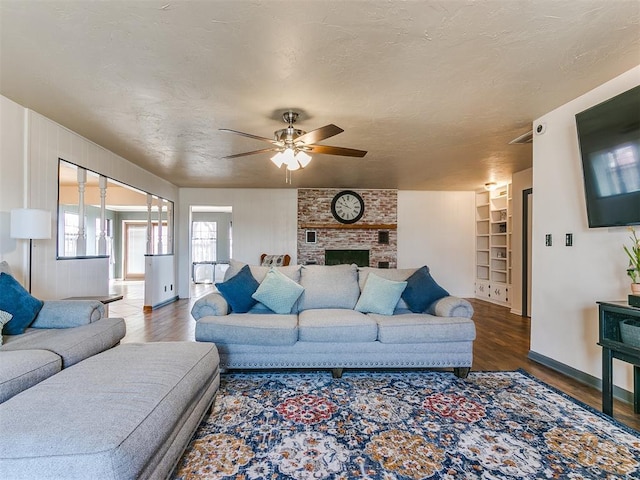 living room featuring built in features, a brick fireplace, a textured ceiling, and wood finished floors