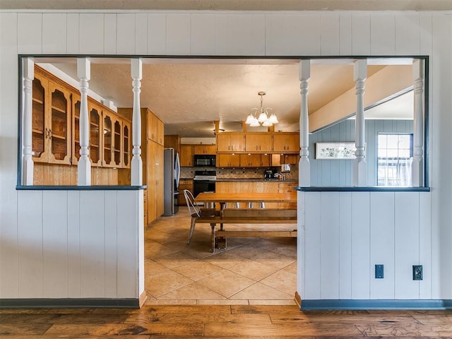 kitchen with black microwave, a chandelier, white range oven, freestanding refrigerator, and brown cabinetry