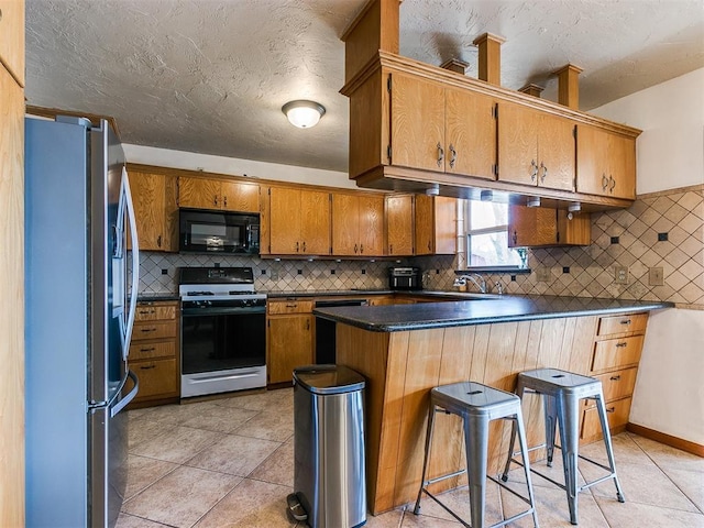 kitchen featuring brown cabinetry, dark countertops, a breakfast bar area, a peninsula, and black appliances