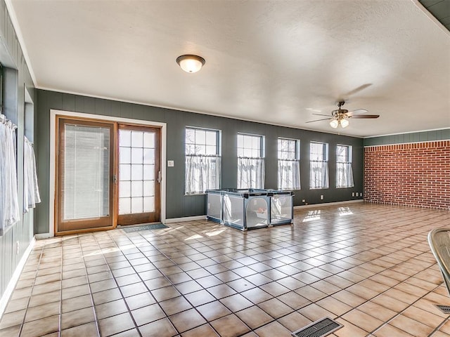 interior space with light tile patterned floors, visible vents, ceiling fan, brick wall, and baseboards