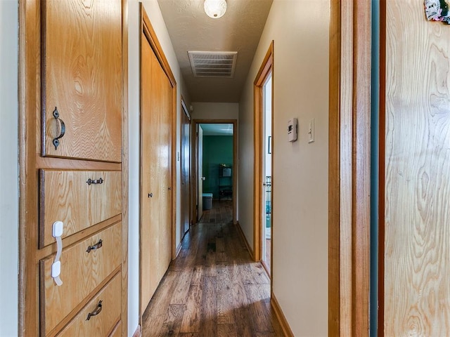 hallway with dark wood-style floors, baseboards, and visible vents