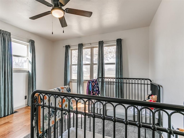 bedroom featuring multiple windows, ceiling fan, baseboards, and wood finished floors